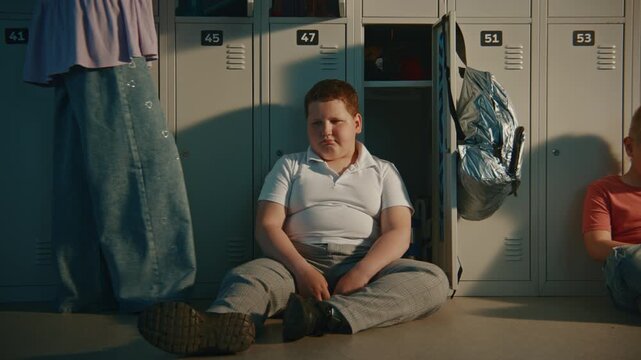 Young Schoolboy Spending Time Alone beside Personal Locker while Classmates Nearby Outside Frame. Concept of Friendship, Social Inclusion, Childhood Emotions, Education, and Student Wellbeing.