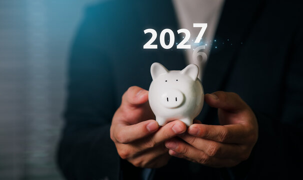 A professional businessman holding a piggy bank with a digital overlay of the year 2027, symbolizing financial growth, investment planning, and future wealth management.