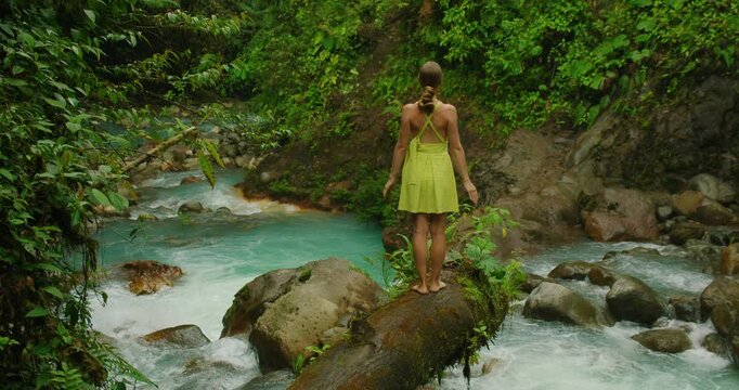 Woman tourist standing on log above turquoise Costa Rica blue water river during summer travel
