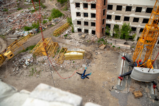 Aerial view of person rope jumping over debris field near abandoned building and construction crane, extreme sport adrenaline concept