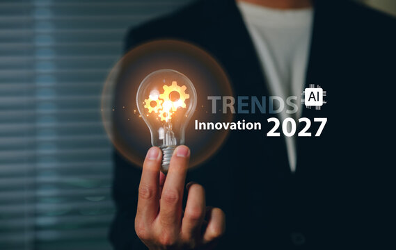 A business professional in formal attire touches a transparent light bulb innovation Trends in 2027 with gears inside, symbolizing innovation, technology, and forward-thinking in a corporate setting.