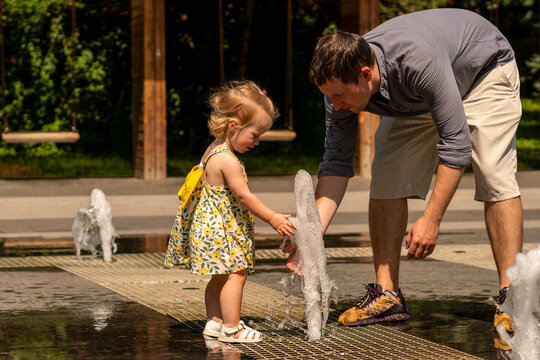 Father Helping Toddler Daughter Touch Ground Fountain Jet