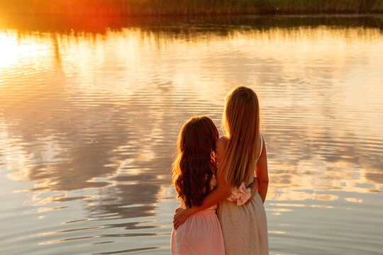 Mother And Daughter Watching Sunset Reflections On Water