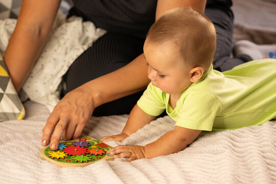 Mother Guides Baby Boy Playing With Wooden Gear Puzzle