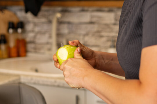 Woman Peels Green Apple With Knife In Home Kitchen