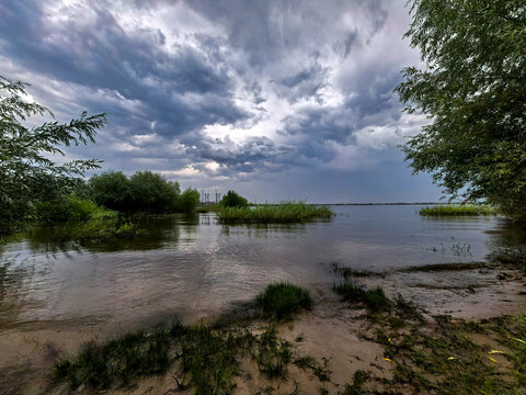 Storm Clouds Gathering Above Wide River And Sandy Shore
