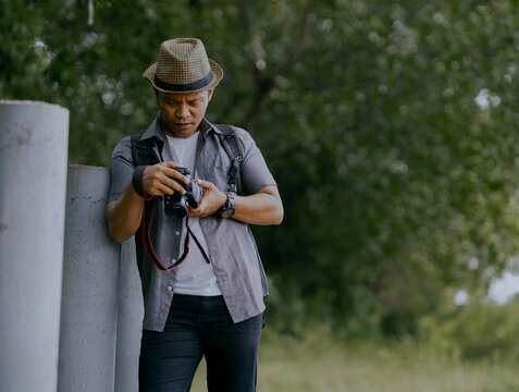 Asian male photographer going through photos on camera in nature.