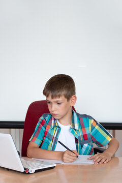 A cute boy is sitting at a table, looking at a laptop, writing homework or preparing for an exam. Concept Back to school