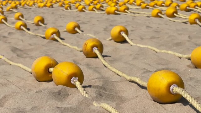 Close up of Round Yellow Buoys on on braided rope neatly laid out in parallel on Sandy Beach. Cinematic Low Angle shot.