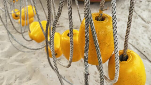 Close Up Yellow Buoys on braided rope swing in the wind above the sandy Beach
