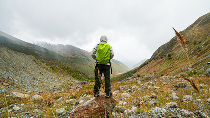 Obraz premium Hiker with green backpack standing on rock looking at autumn mountain valley near Shkhara glacier in Georgia.