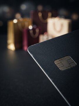 Close Up of Black Credit Card with EMV Chip and Blurred Luxury Shopping Bags