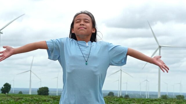 Happy young girl standing with open arms embracing nature with wind turbines in background