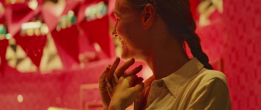 Woman with hands clasped gazing at illuminated luxury display at bright boutique