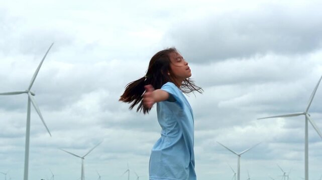 Happy young girl standing with open arms embracing nature with wind turbines in background