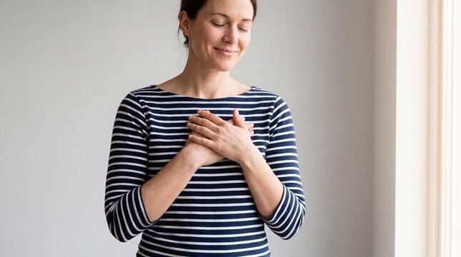 Woman with eyes closed holding hands over heart feeling gratitude and peace.