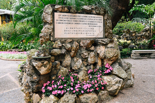 MACAU, CHINA, APRIL 1 2026, Historic stone monument with portuguese and chinese memorial plaque in lou lim ioc garden surrounded by blooming flower