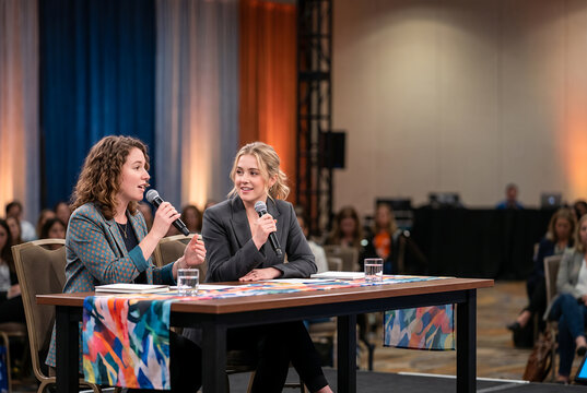 Two women laughing together at conference table with microphones