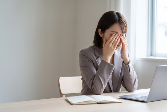 Asian woman in office holding head stressed during work at desk
