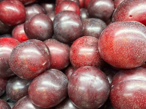 Full frame close-up pattern of fresh organic ripe dark red black plums displayed at a market