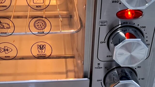 Close up view of a kitchen oven interior with glowing heating elements and control dials set for cooking different food items
