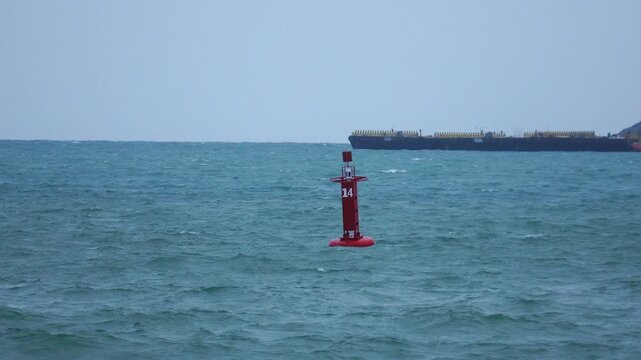 Red navigation sea buoy floating in blue ocean with large cargo ship passing in background