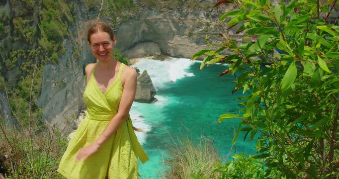 Woman in dress smiles atop high cliff overlooking Diamond Beach in Nusa Penida Island Bali Indonesia