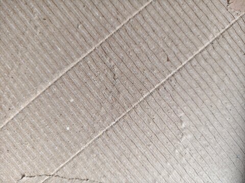 Corrugated cardboard surface with faint parallel lines and textured creases, providing a rough brown backdrop for creative projects and packaging design.