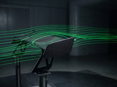 Carbon fiber automotive rear wing spoiler tested in a wind tunnel with green laser streamlines visualizing aerodynamic airflow