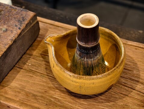Close-up of a traditional Japanese bamboo whisk (chasen) inside a crafted yellow ceramic matcha bowl. Perfect for tea ceremony, organic matcha, healthy lifestyle, and cafe culture concepts