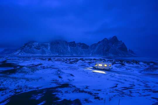 Cozy camper van parked on snowy Stokksnes beach at night with majestic Vestrahorn mountain in Iceland.
