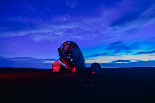 Dramatic night view of the famous DC-3 plane wreck at Solheimasandur black sand beach in Iceland with neon red lighting against twilight sky.