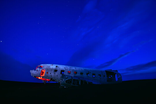 Dramatic night view of the famous DC-3 plane wreck at Solheimasandur black sand beach in Iceland with neon red lighting against twilight sky.