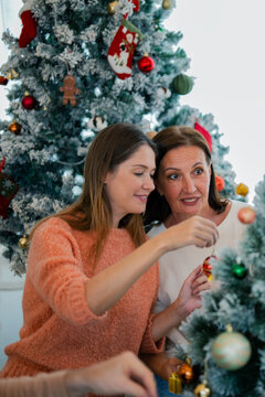 Daughter decorating Christmas tree with senior mother beside her, sharing warm family moments and holiday tradition together at home.
