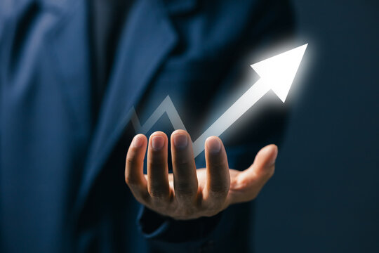 Business person holding glowing upward arrow, representing financial growth, business success, increasing profit, positive performance, development, progress and strategic achievement.