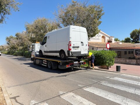 Palma, spain, august 2, 2026, tow truck operator loading a broken down white delivery van onto a flatbed for transport and recovery service