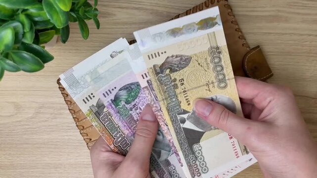 A close-up of a woman's hands removing Cambodian riels from a leather wallet and counting the cash. Using Cambodia's national currency in everyday financial transactions.