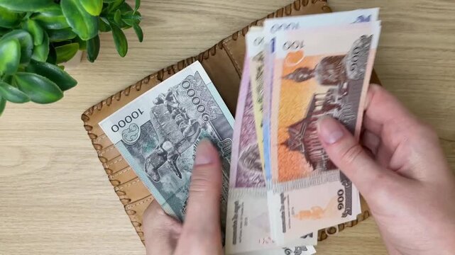 A close-up of a woman's hands counting Cambodian riels. Concepts for personal finance, money transactions, budgeting, and using Cambodia's national currency.