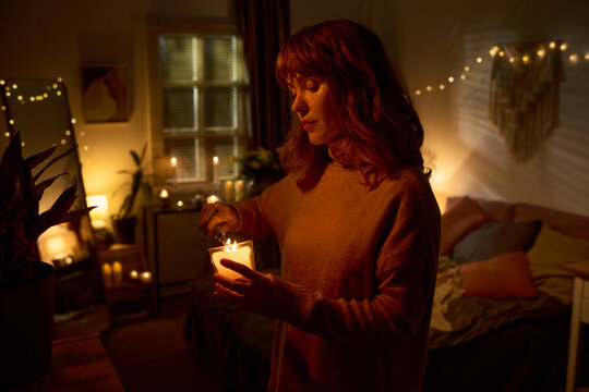 Caucasian young adult woman lighting candle in bedroom, practicing self care and mindfulness. Image represents mental wellbeing and relaxation, suitable for lifestyle marketing