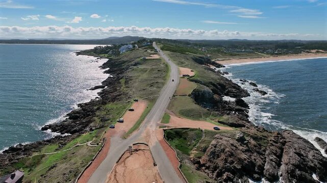 Punta Ballena peninsula road with rocky coastlines on both sides, forward push aerial on a clear day in Uruguay.