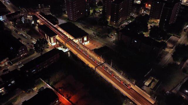 Bruce Grove railway station and Tottenham High Road form a brightly lit transport corridor through Tottenham, Haringey, with apartment blocks and streets, drone descending.
