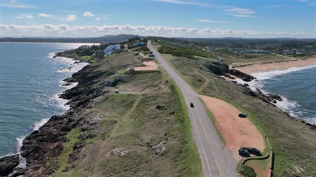 Punta Ballena coastal road forward push along a grassy ridge with ocean views on both sides and a sandy beach visible to the right.