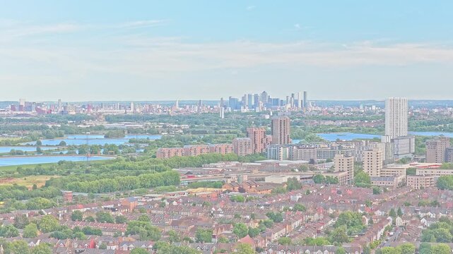 Tottenham residential district stretches toward Lee Valley reservoirs, with dense terraced housing and London's high-rise skyline beyond, drone ascending.