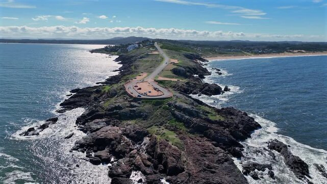 Punta Ballena aerial forward push along the narrow peninsula road with cars, tourists, and ocean on both sides in Uruguay