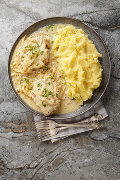 German schnitzel with onion cream sauce and mashed potatoes garnish close-up in a plate on the table. Vertical top view from above