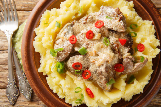 Homemade fried liver with onions and sour cream served with mashed potatoes close-up in a plate on the table. Horizontal top view from above