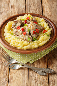 Fried liver with onions and sour cream served with mashed potatoes close-up in a plate on the table. Vertical