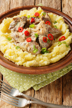Chicken liver in cream sauce with mashed potatoes closeup on thr plate on the wooden table. Vertical
