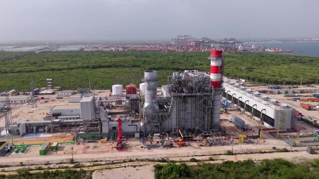 Wide aerial view of a natural gas power plant under construction with turbines exhaust stacks and engineering infrastructure near the Caribbean coast