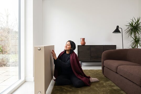 Woman warming her hands at the radiator in a bright living room in winter